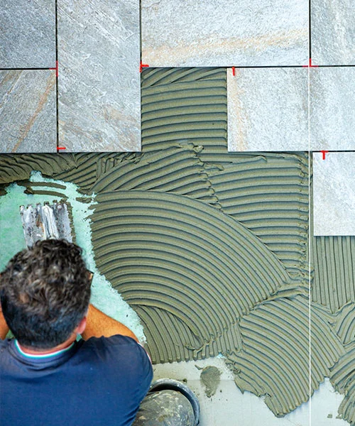 Worker installing tiles with adhesive on an industrial flooring project, showcasing precise alignment and professional craftsmanship.